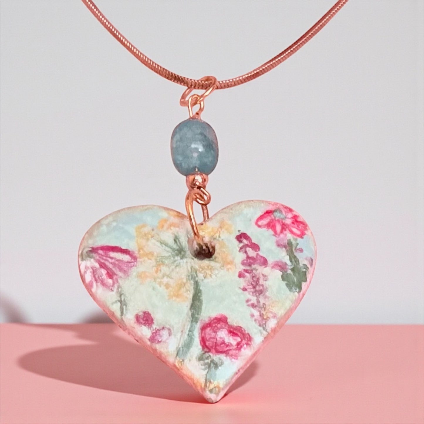 Heart-shaped floral pendant on a pink surface with a light gray background
