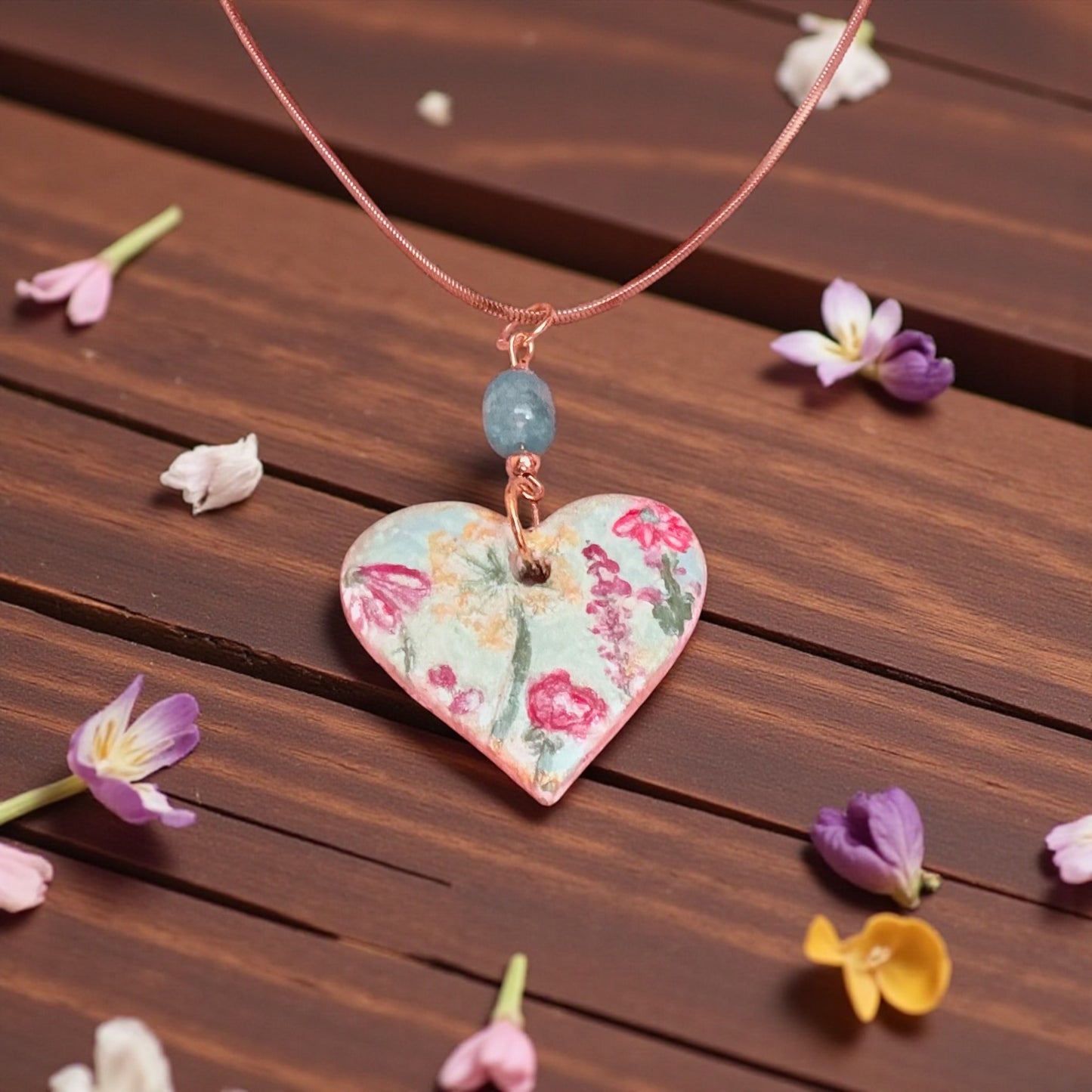 Heart-shaped floral pendant necklace on a wooden surface with small flowers around