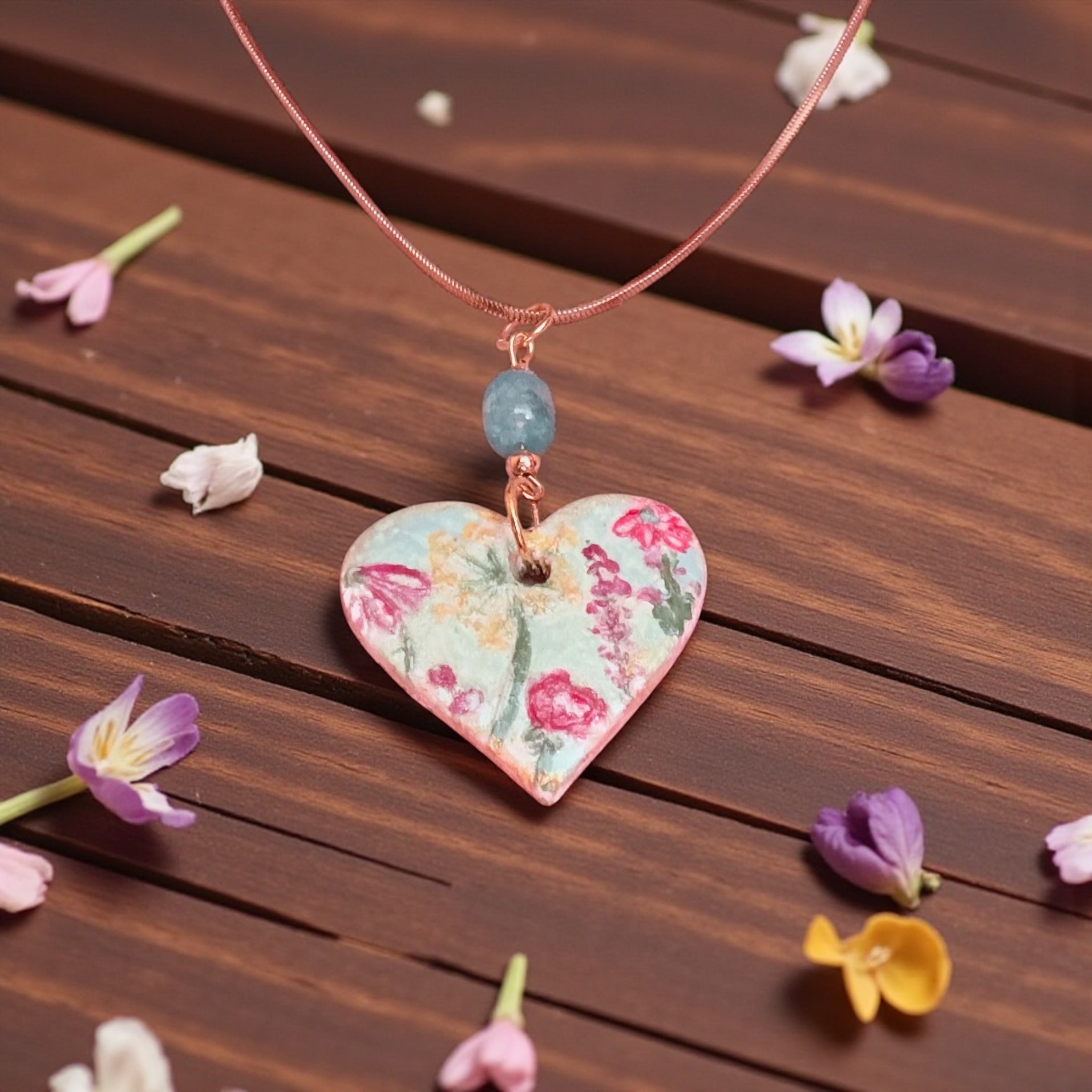Heart-shaped floral pendant necklace on a wooden surface with small flowers around