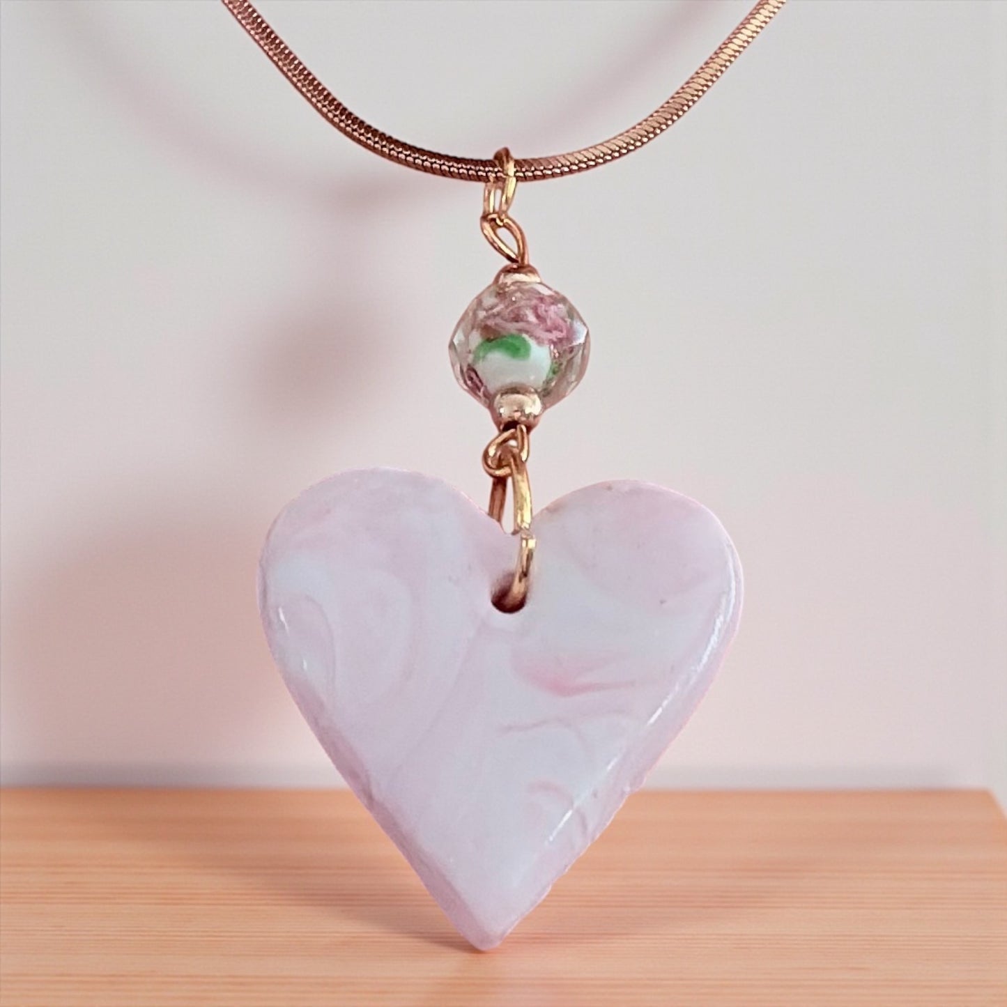 Heart-shaped pink pendant with a floral bead on a wooden surface