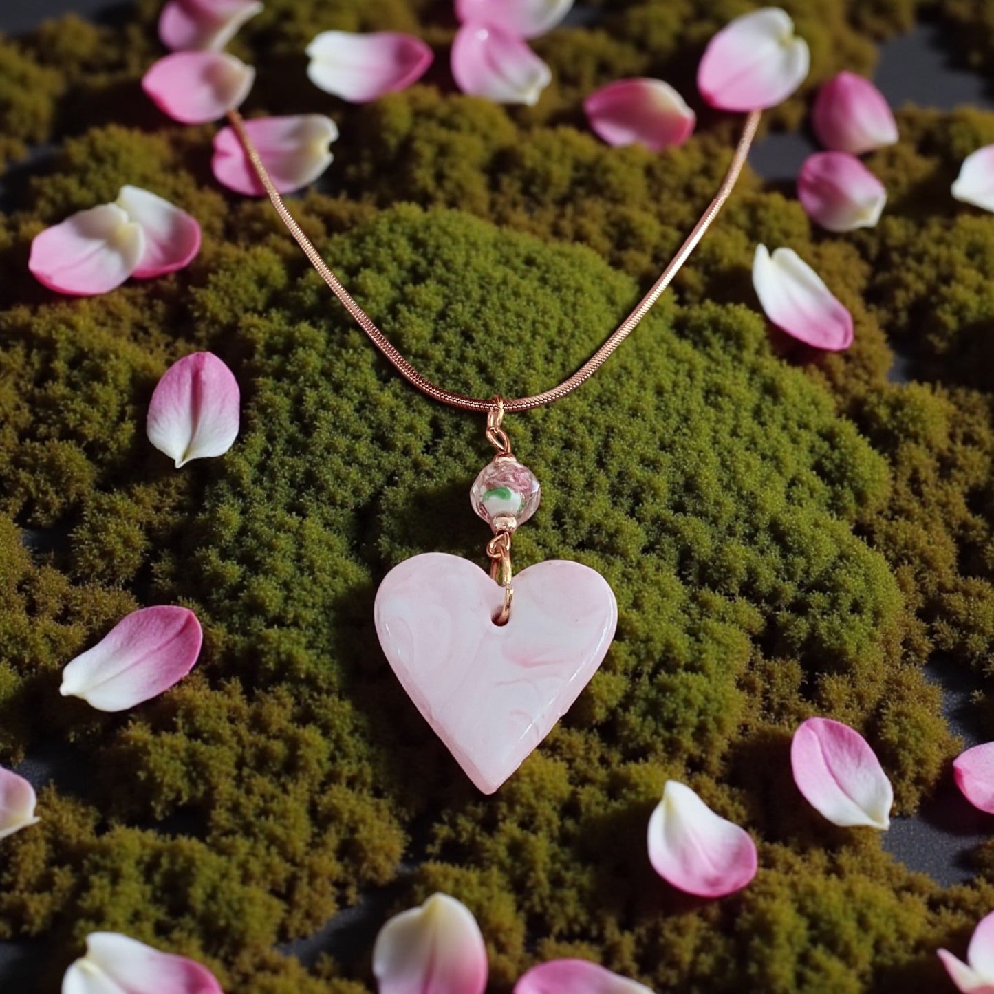 Heart-shaped pink pendant necklace on a moss background with pink petals