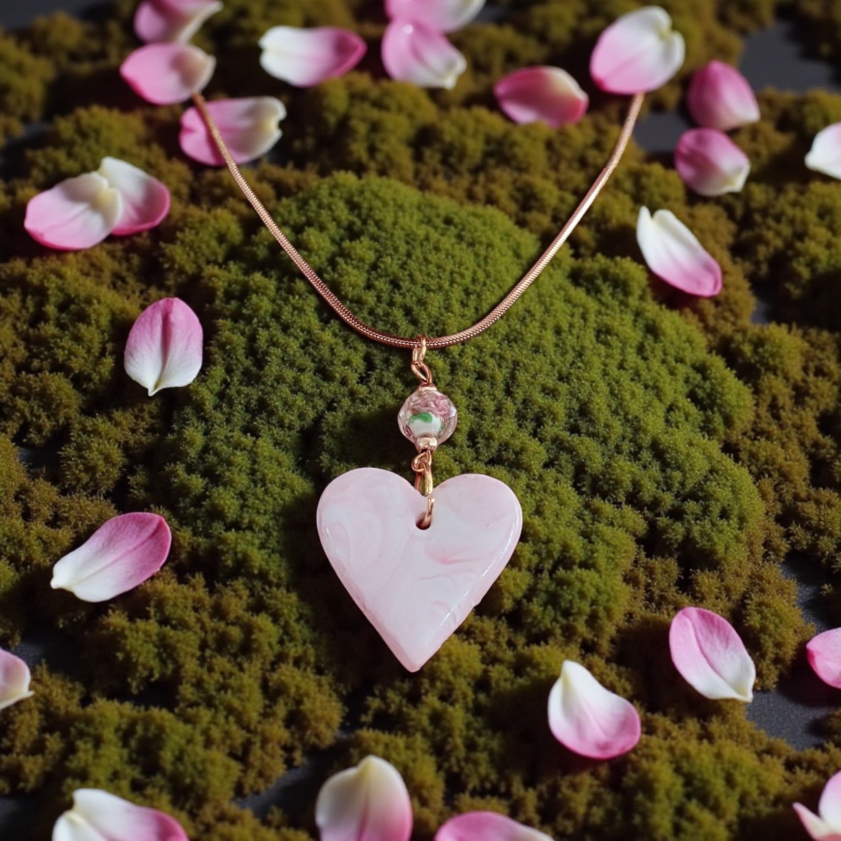 Heart-shaped pink pendant necklace on a moss background with pink petals